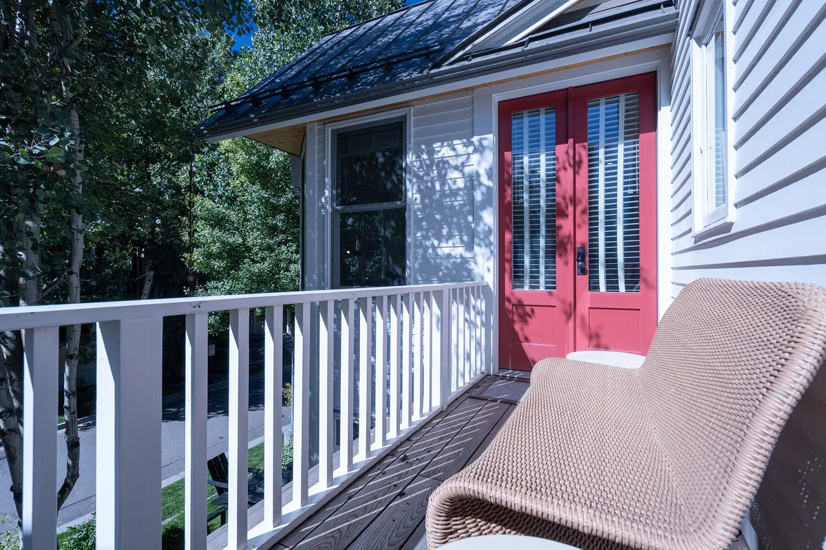 This image features a charming exterior view with red doors, a woven lounge chair, and a wooden balcony, framed by calm surroundings. The setup invites relaxation and offers a glimpse into outdoor spaces that families can enjoy together or separately.