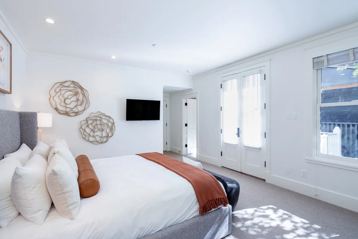 A sophisticated bedroom with a king-sized bed, decorative pillows, stylish wall art, modern lighting, and a mounted TV. The room is bathed in natural light, creating a tranquil and inviting environment ideal for relaxation after a day of adventure.