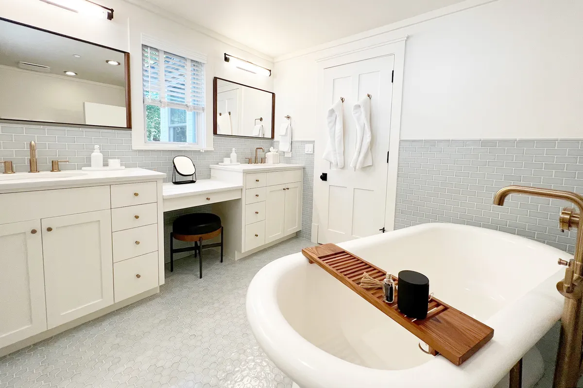 A luxurious en suite bathroom featuring a freestanding soaking bathtub, dual vanities with mirrors, and a wooden bath tray. The space is styled for spa-like relaxation, with soft lighting and a tranquil ambiance ideal for unwinding.