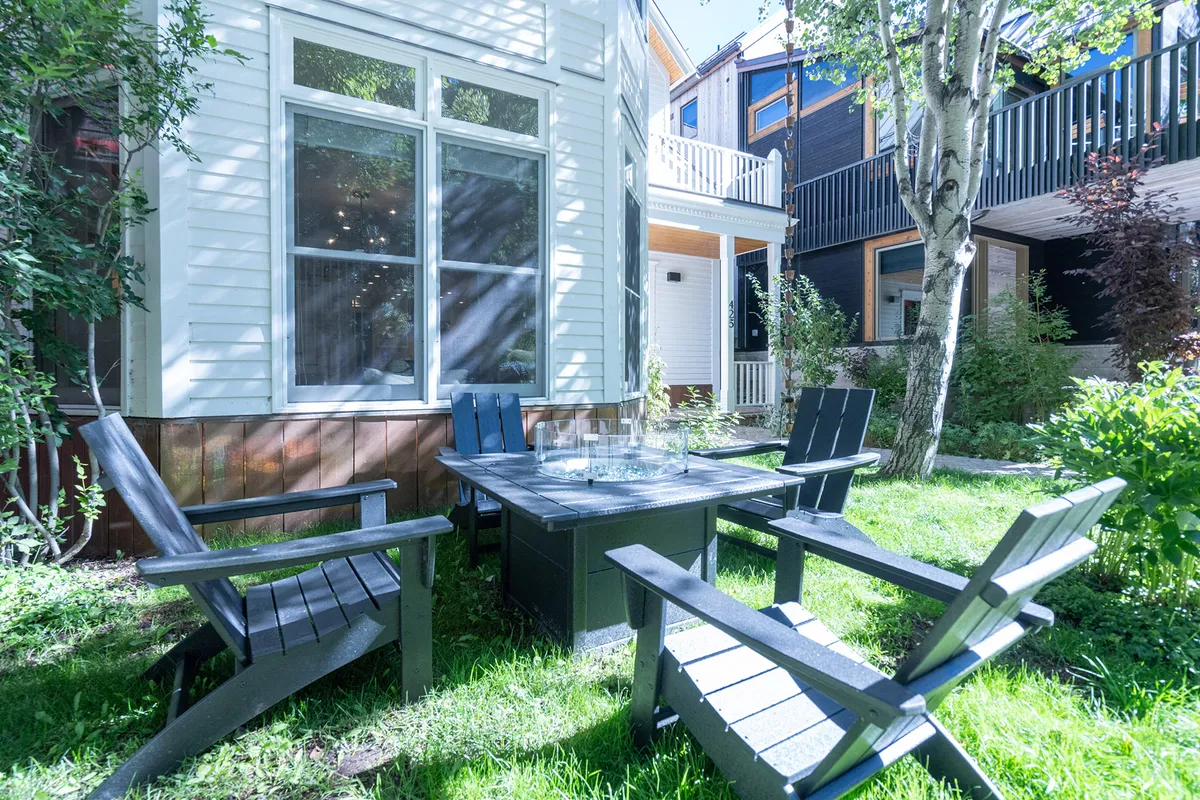 A welcoming exterior seating area featuring a large dining table surrounded by comfortable chairs. Lush greenery frames the space, and the area is designed for social gatherings, outdoor dining, and relaxation. The inviting fire pit hints at evenings spent under the stars, sharing stories or roasting marshmallows.