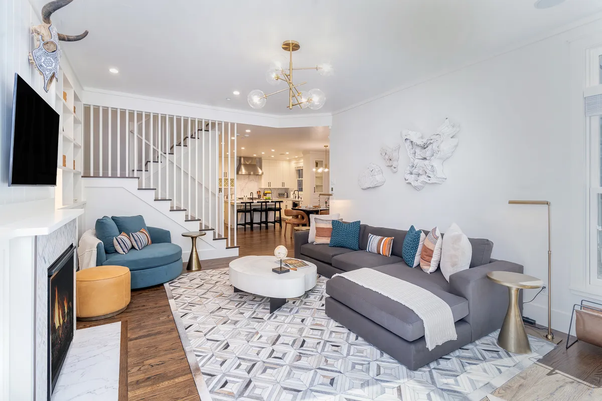 A warm, open living room featuring a comfortable sofa, a cozy fireplace, a stylish coffee table, and a staircase leading to another level. The space is arranged for both relaxation and conversation, with ample natural light streaming in.