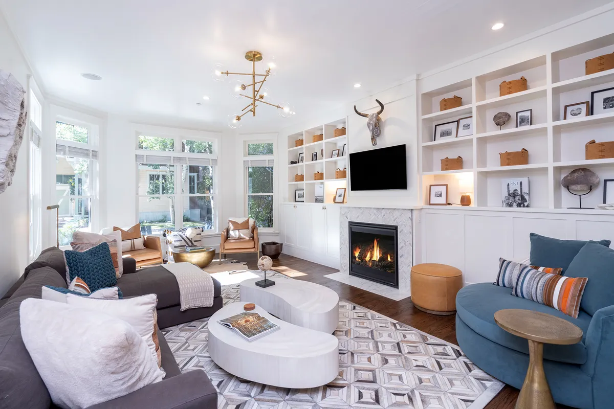 A bright and inviting living room with a modern fireplace as the centerpiece, surrounded by sleek built-in shelves filled with curated decor. A plush sofa and stylish coffee table invite guests to gather, with sunlight streaming through large windows to create a warm, welcoming atmosphere. The scene exudes both contemporary elegance and cozy comfort, ideal for relaxing after a day on the slopes.