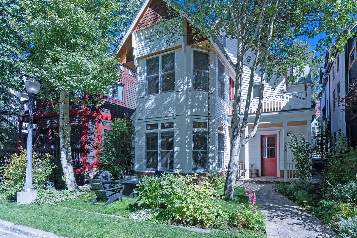 A bright and inviting view of the home's exterior with large windows, a vibrant red door, a landscaped garden, and a patio seating area. The image captures the welcoming feel of the front yard and showcases the patio space as an ideal spot to relax and enjoy the natural surroundings.