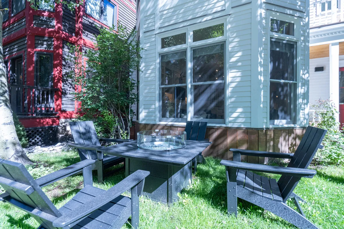 This image showcases an outdoor seating area with a fire pit, surrounded by lush greenery and adjacent colorful houses. The seating setup encourages gatherings, relaxation, and fireside chats, making it a central hub for both socializing and unwinding outdoors.