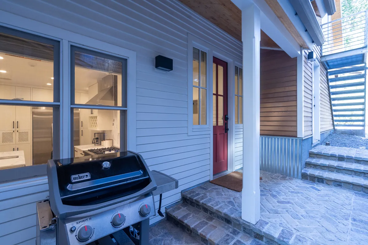 An inviting exterior view showcasing a grill and red door, with a stone pathway leading to the entrance. This space is set up for outdoor cooking and gathering, inviting residents and guests to enjoy al fresco meals in the fresh mountain air.