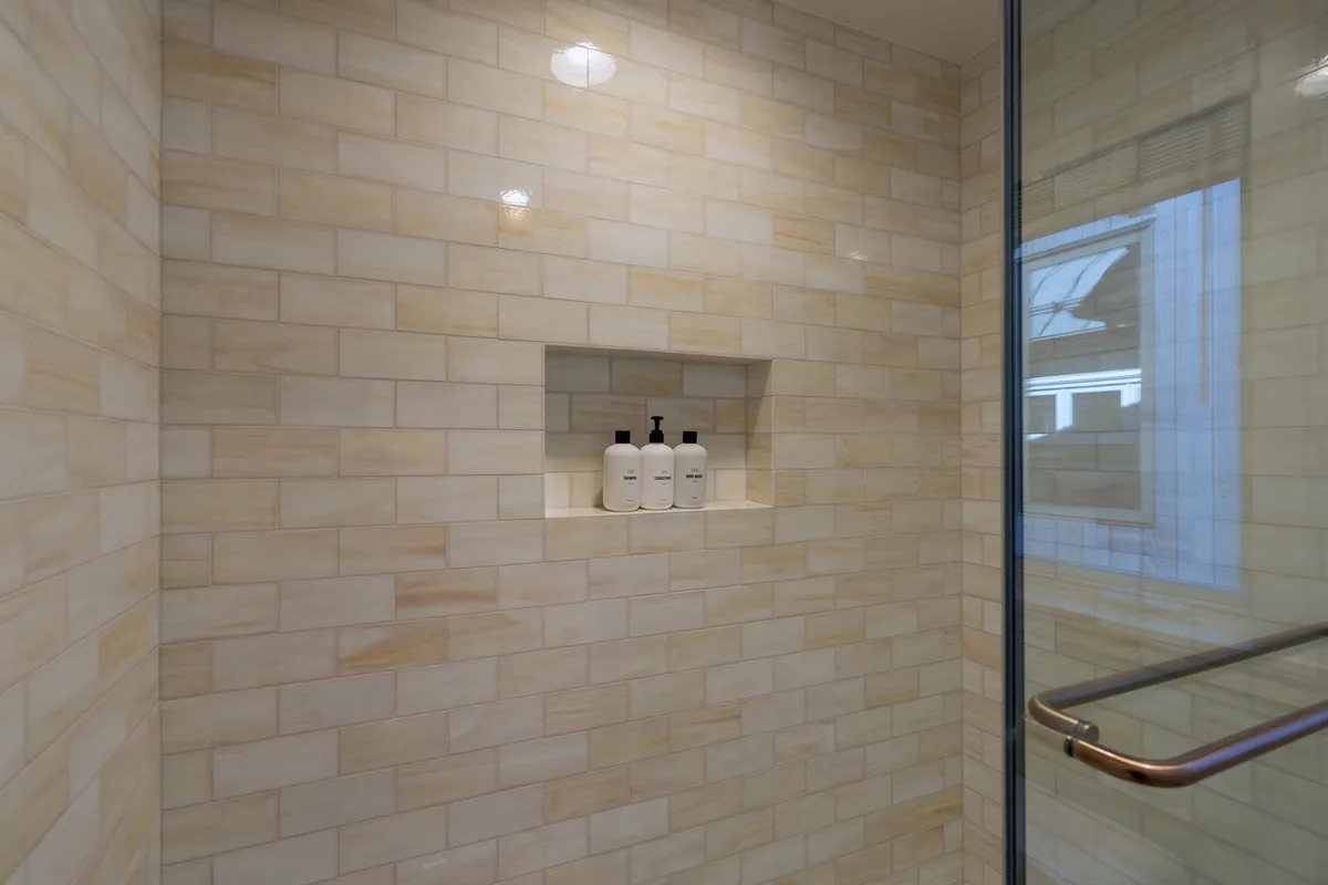 A modern, refreshing shower area with glass enclosure and neatly arranged bath products on a shelf. The space feels clean, bright, and functional—ideal for kids needing a quick shower after a busy day of play.