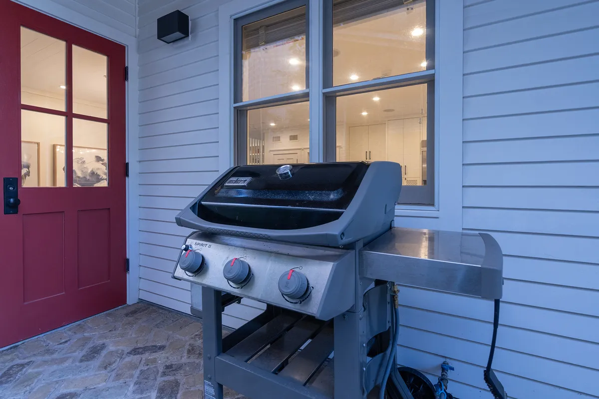 A view of the home's exterior showing a grill, red door, and window, suggesting a relaxed setting for outdoor meals and socializing. The scene is casual and welcoming, hinting at the family barbecues and group activities that the space can host.